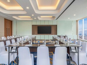A conference room with a long table, white chairs, and a large screen. - Novotel Jakarta Pulo Mas (Jakarta)