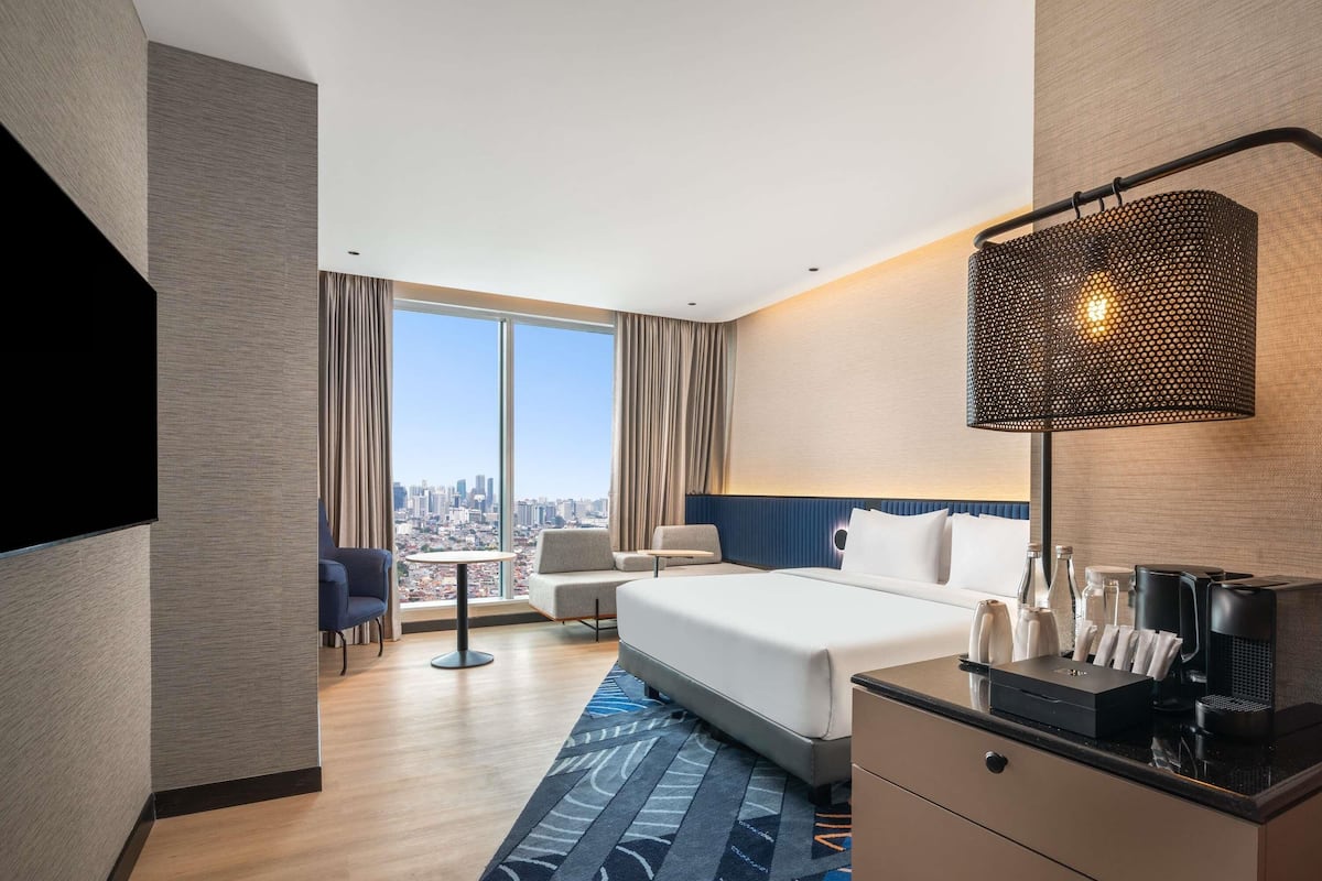 Una habitación de hotel con una cama grande, un escritorio, una silla, un televisor y vistas a la ciudad.