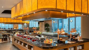 A modern restaurant with a buffet setup, large windows, and a city view.