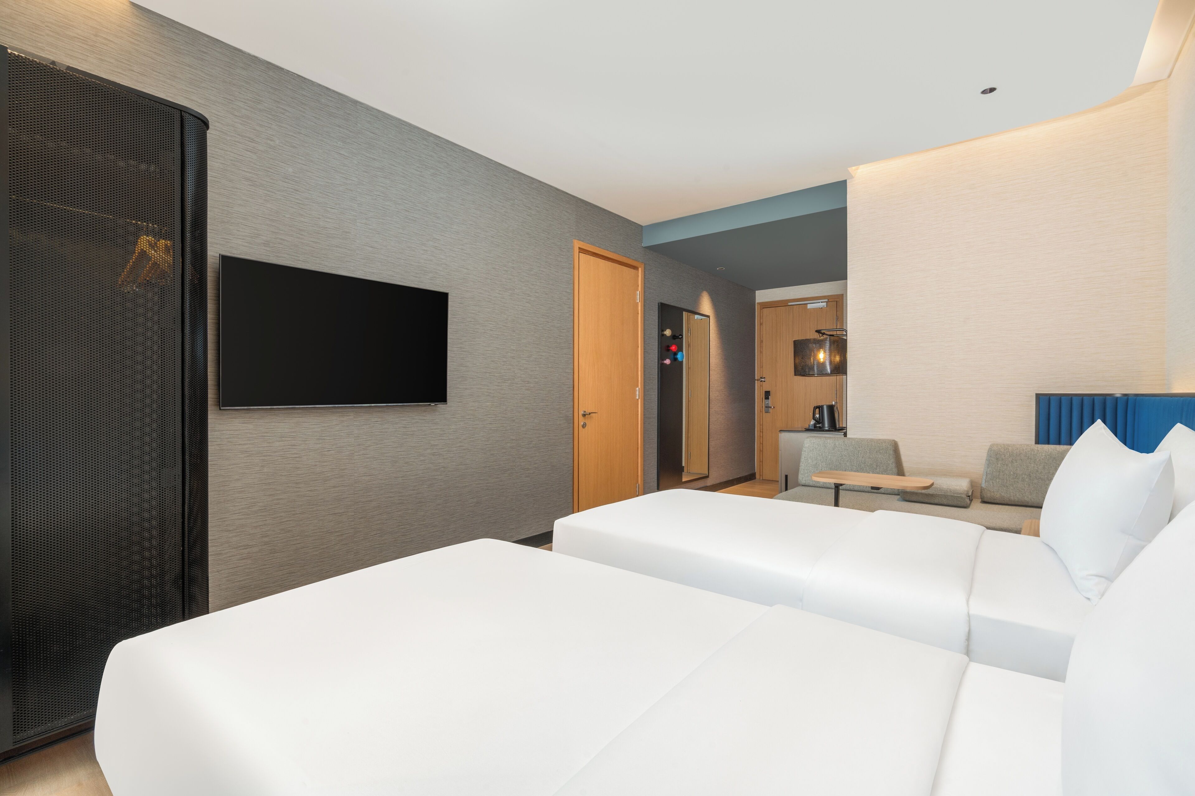 A modern hotel room with a large bed, a TV mounted on the wall, and a seating area with a small table and chairs.