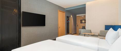 Ein modernes Hotelzimmer mit einem großen Bett, einem an der Wand montierten Fernseher und einer Sitzecke mit einem kleinen Tisch und Stühlen.