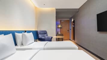 A modern hotel room with a bed, a blue armchair, a small table, and a TV mounted on the wall.