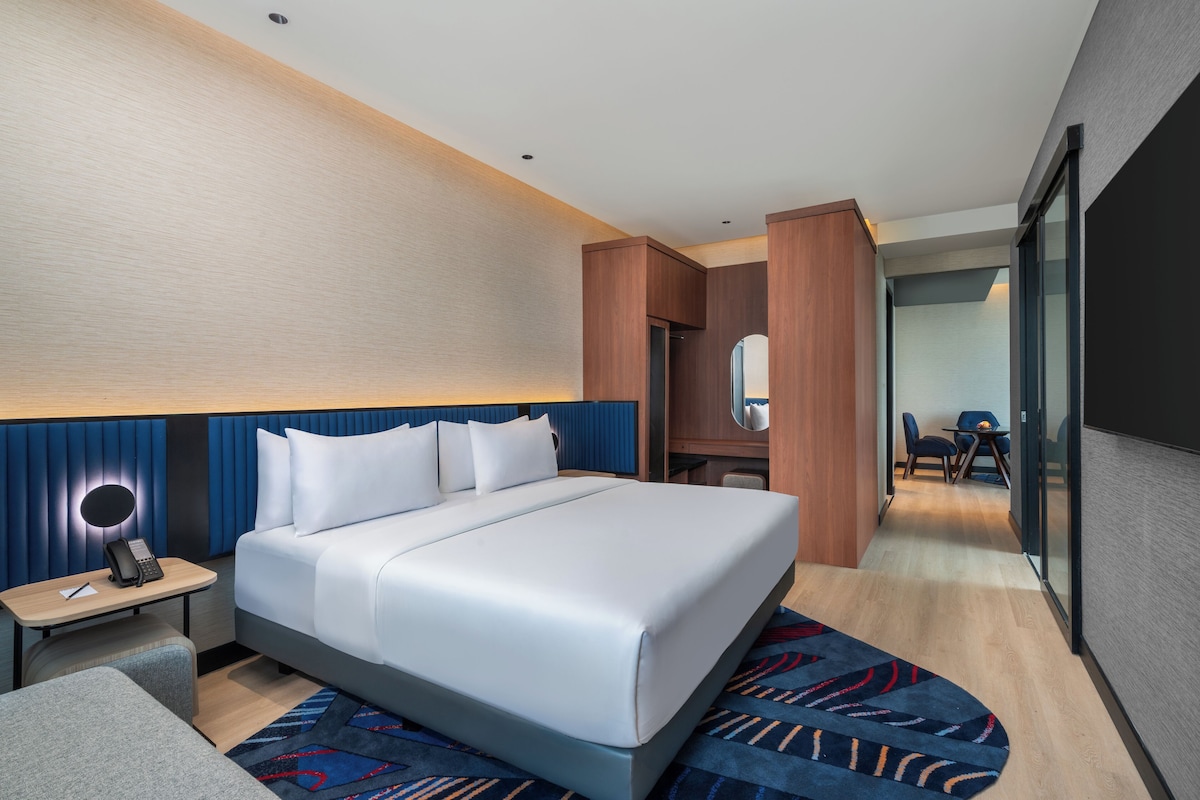 Ein modernes Hotelzimmer mit einem großen Bett, einem Nachttisch mit Lampe, einem Schreibtisch und einem Sessel.