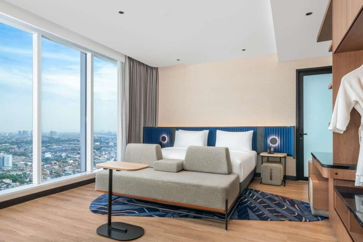 Ein modernes Hotelzimmer mit einem großen Bett, einem kleinen Tisch, einem Nachttisch und Blick auf die Stadt.