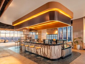 Zona de bar moderna con techo curvo, taburetes y una vitrina con postres.