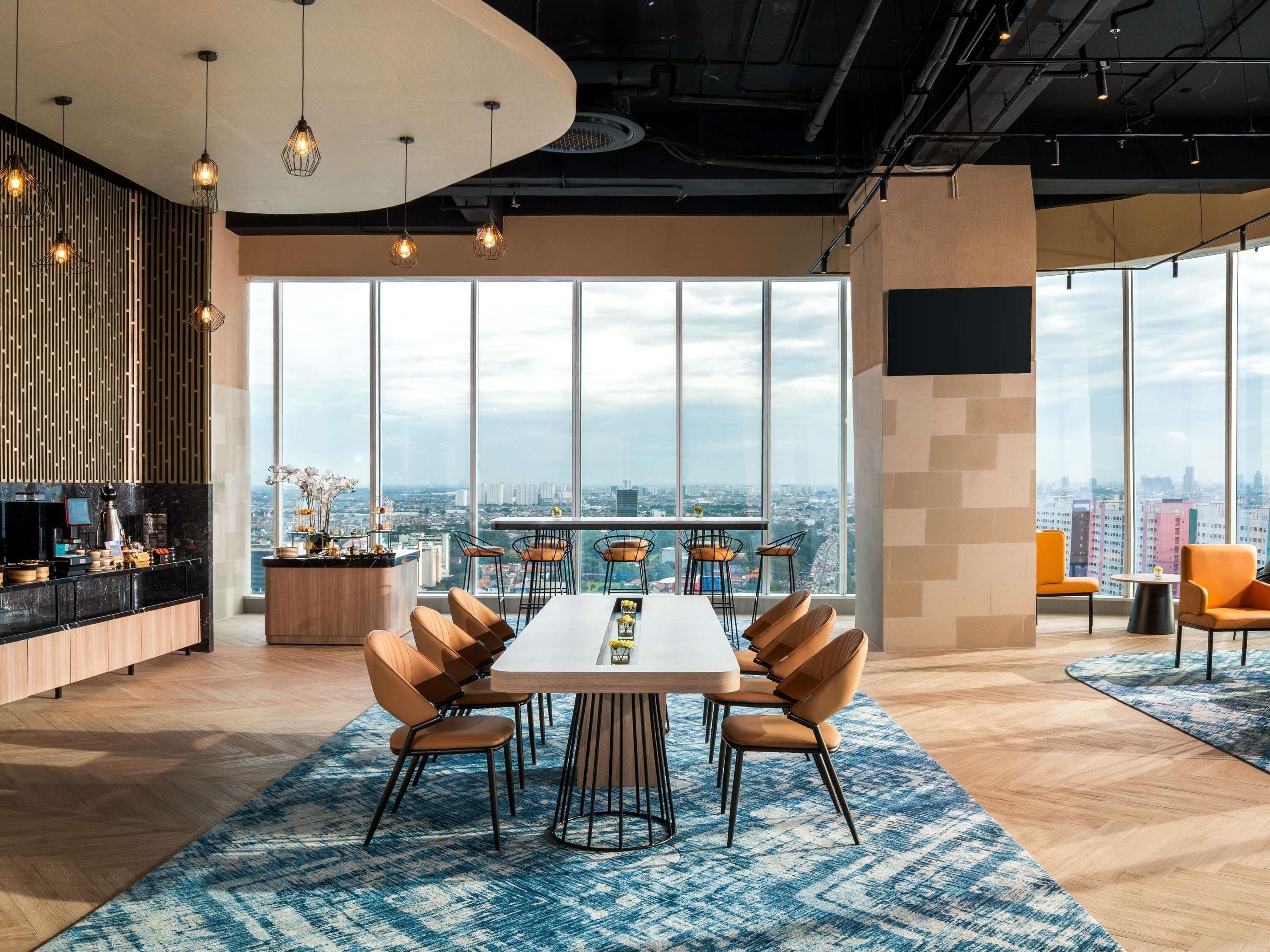 Ein moderner Arbeitsbereich mit großem Tisch und Stühlen, einer Bar und großen Fenstern mit Blick auf die Stadt.