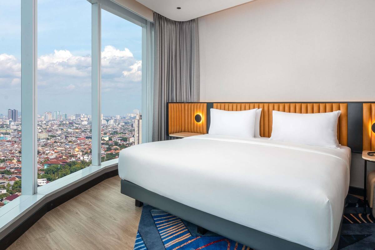 Habitación de hotel con una cama grande, vistas a la ciudad y un diseño moderno.