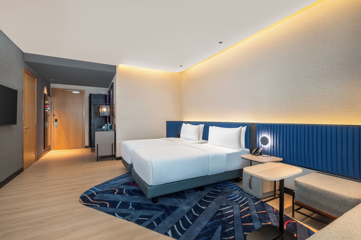 Ein modernes Hotelzimmer mit einem großen Bett, einem kleinen Schreibtisch, einem Stuhl und einem Fernseher.