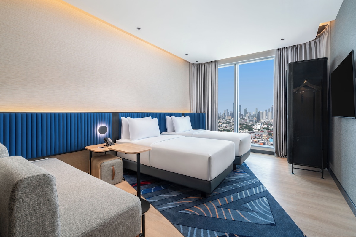 Ein modernes Hotelzimmer mit einem großen Bett, einem Schreibtisch, einem Sessel und einem Fernseher.