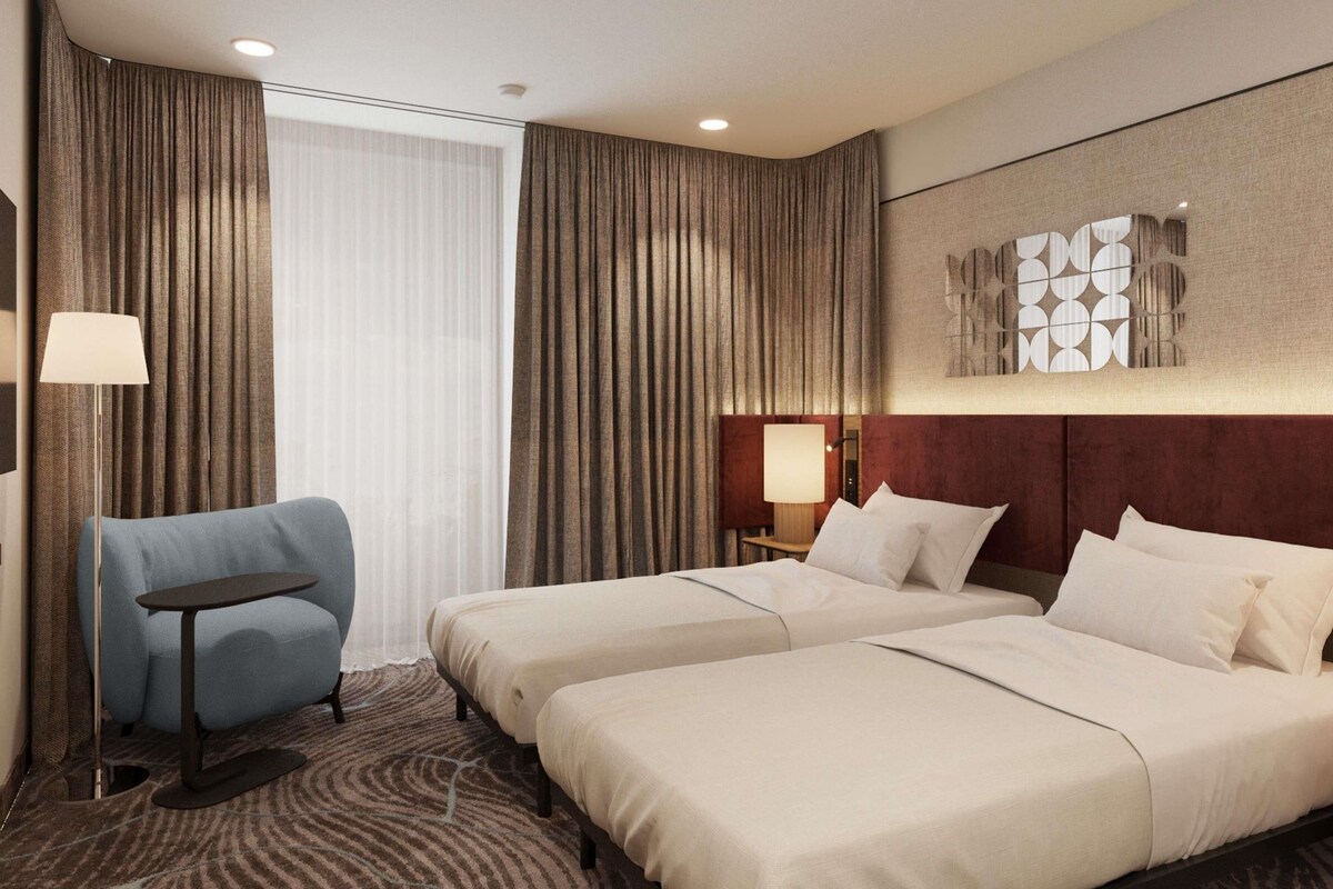 A hotel room with two beds, a desk, a chair, and a large window with curtains.