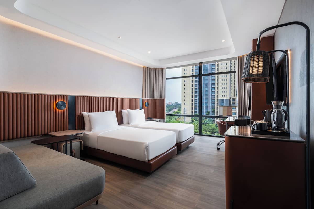 Una habitación de hotel moderna con un ventanal grande, una cama, un sofá y un escritorio con lámpara.