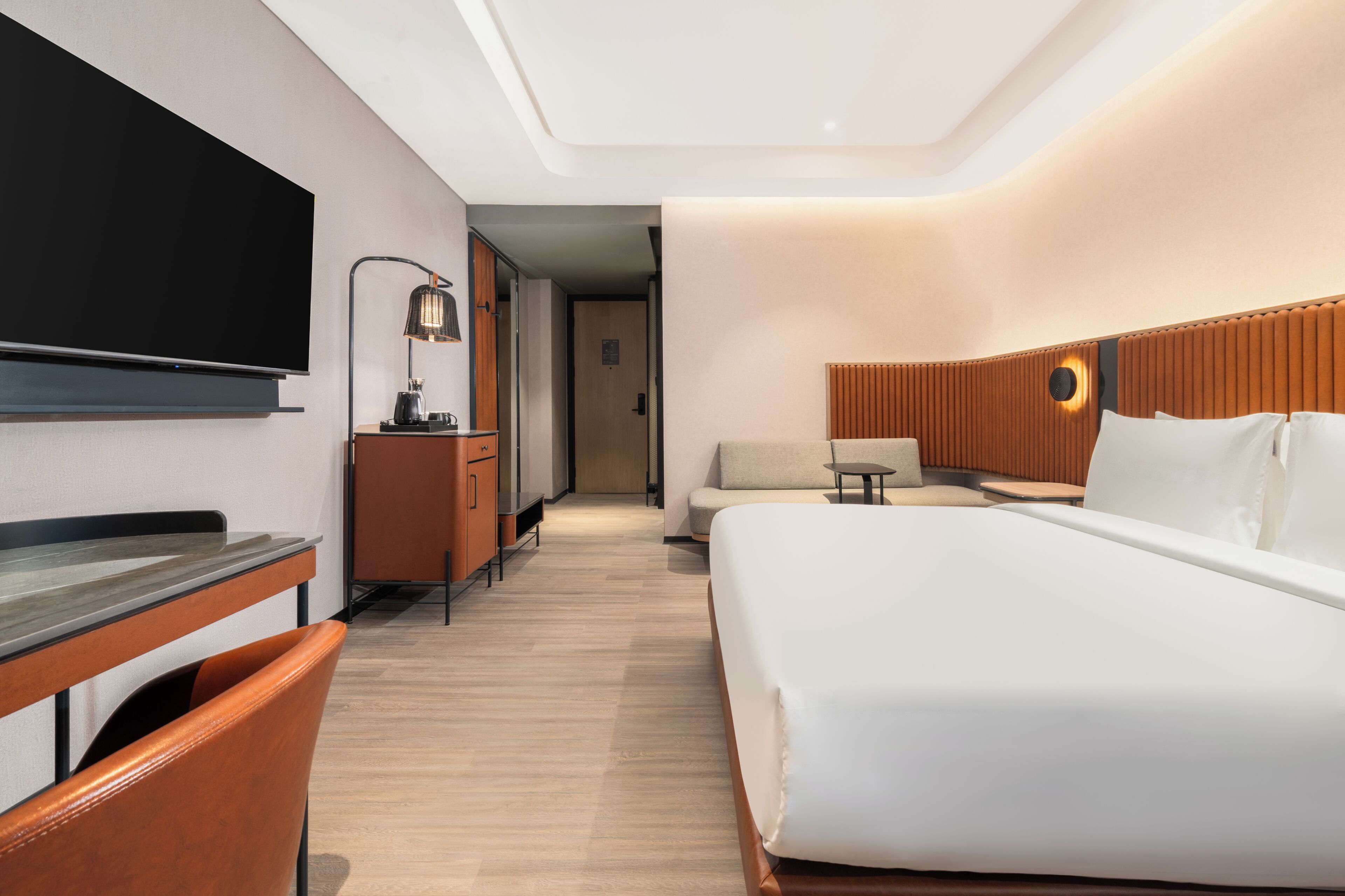 A hotel room with a bed, a desk, a chair, a TV, a lamp, and a small table.
