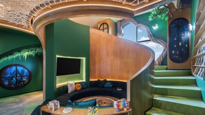 A curved wooden staircase leading to a seating area with a round table, a large window, and a bookshelf. - Novotel Tangerang Bsd City (Pagedangan)