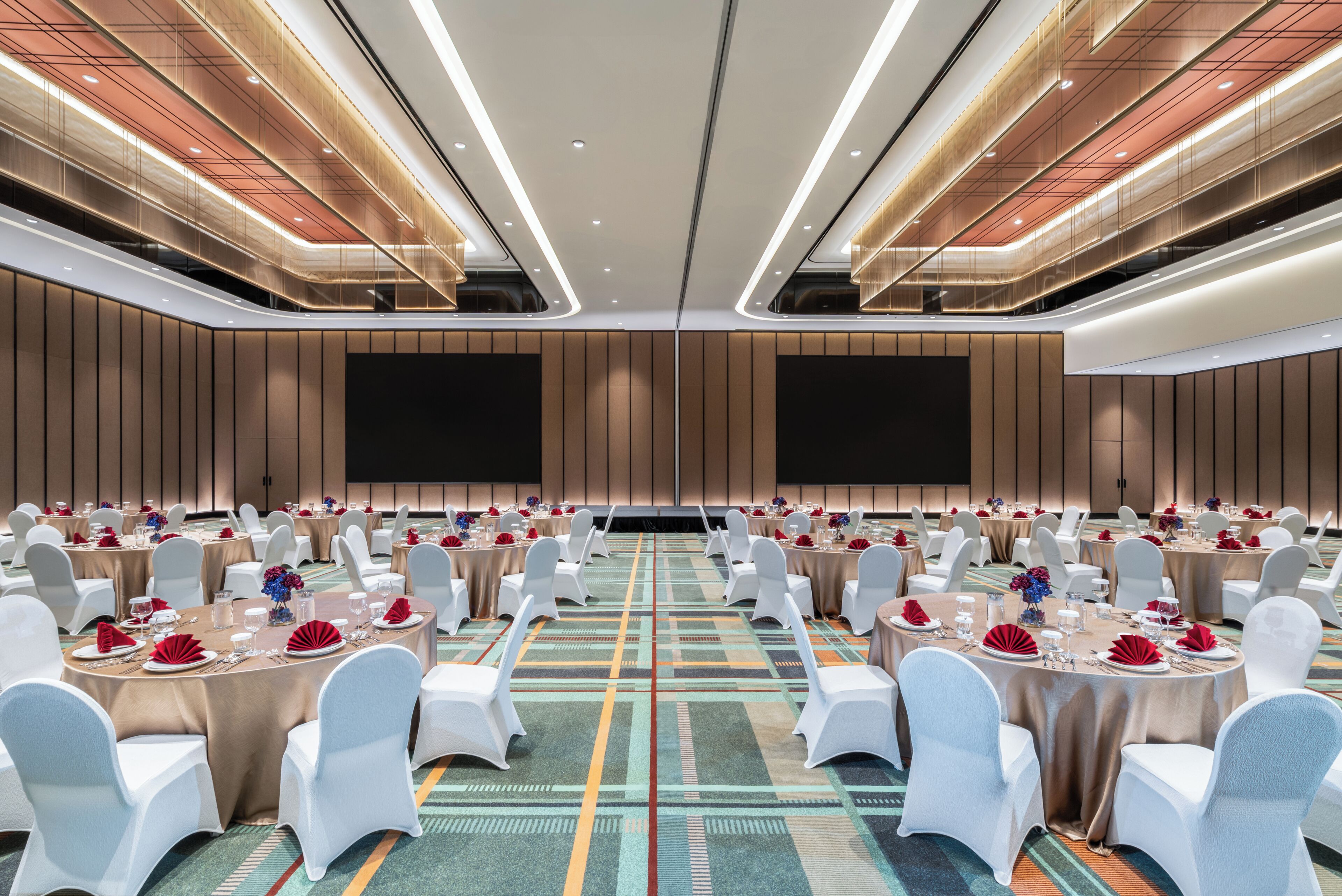 Un salón de conferencias con mesas redondas, sillas blancas y suelo alfombrado.