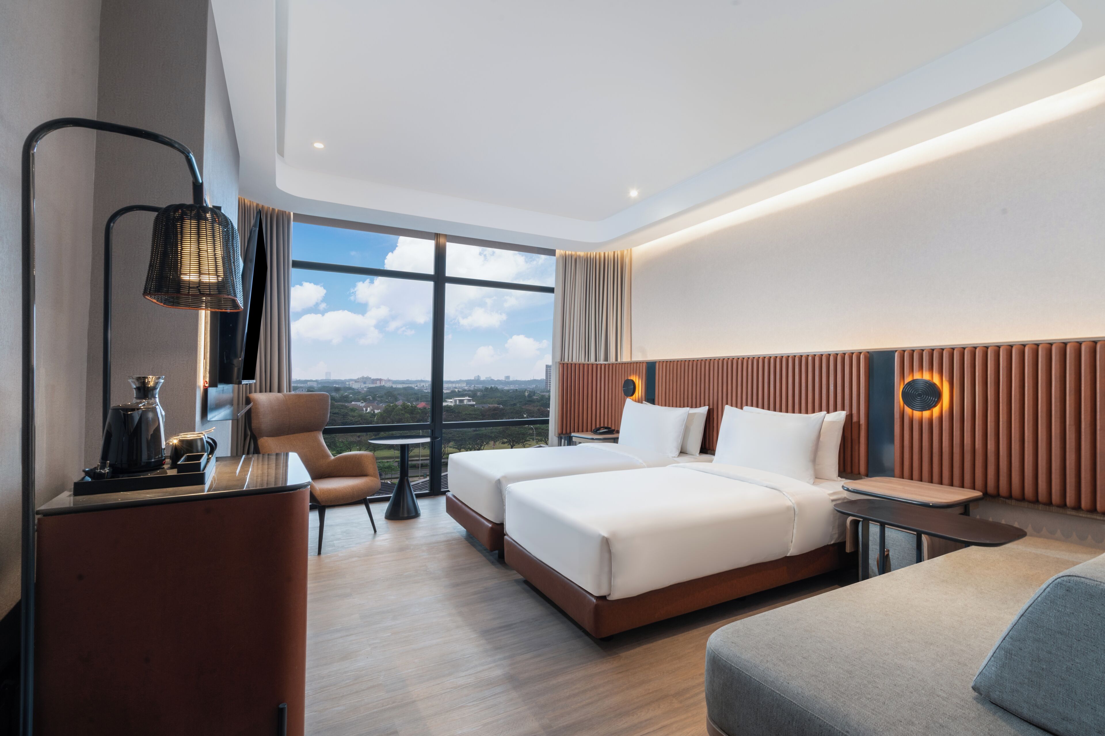A modern hotel room with a large window, a bed, a desk, a chair, and a sofa.