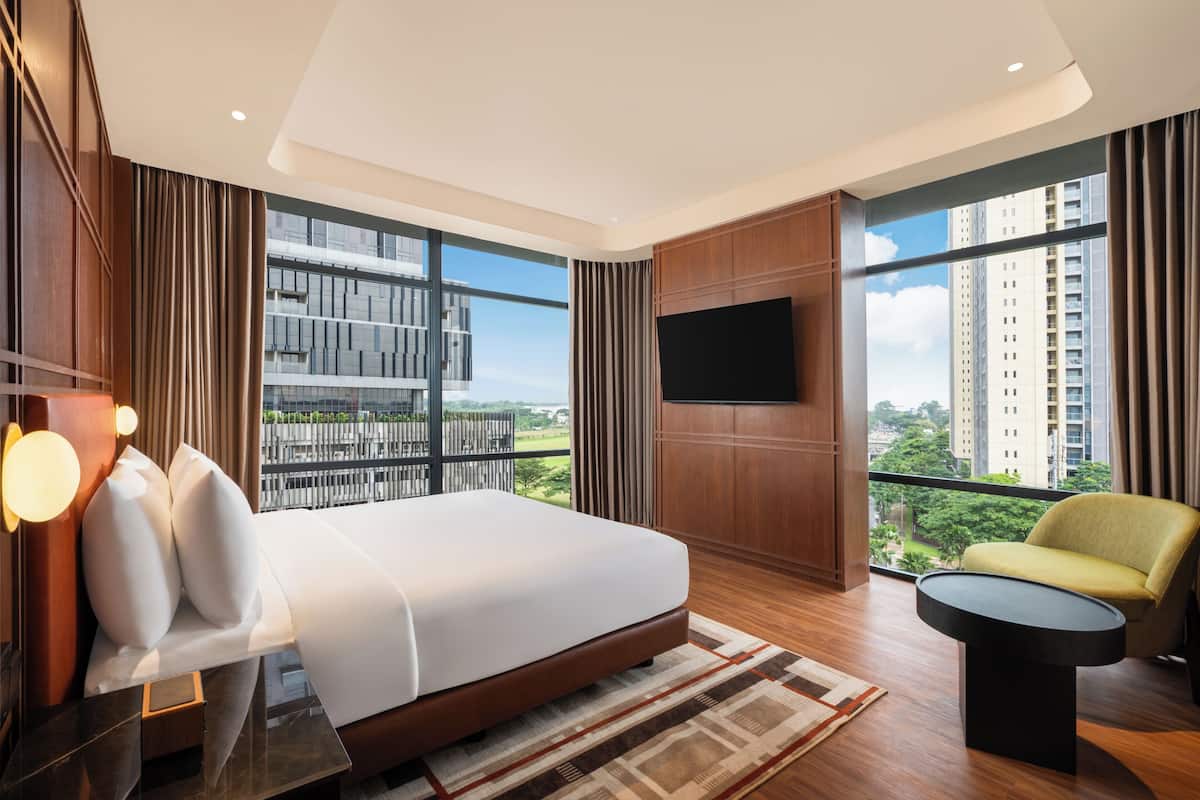 Una habitación de hotel moderna con una cama grande, un televisor de pantalla plana, un sofá y vistas a un paisaje urbano.