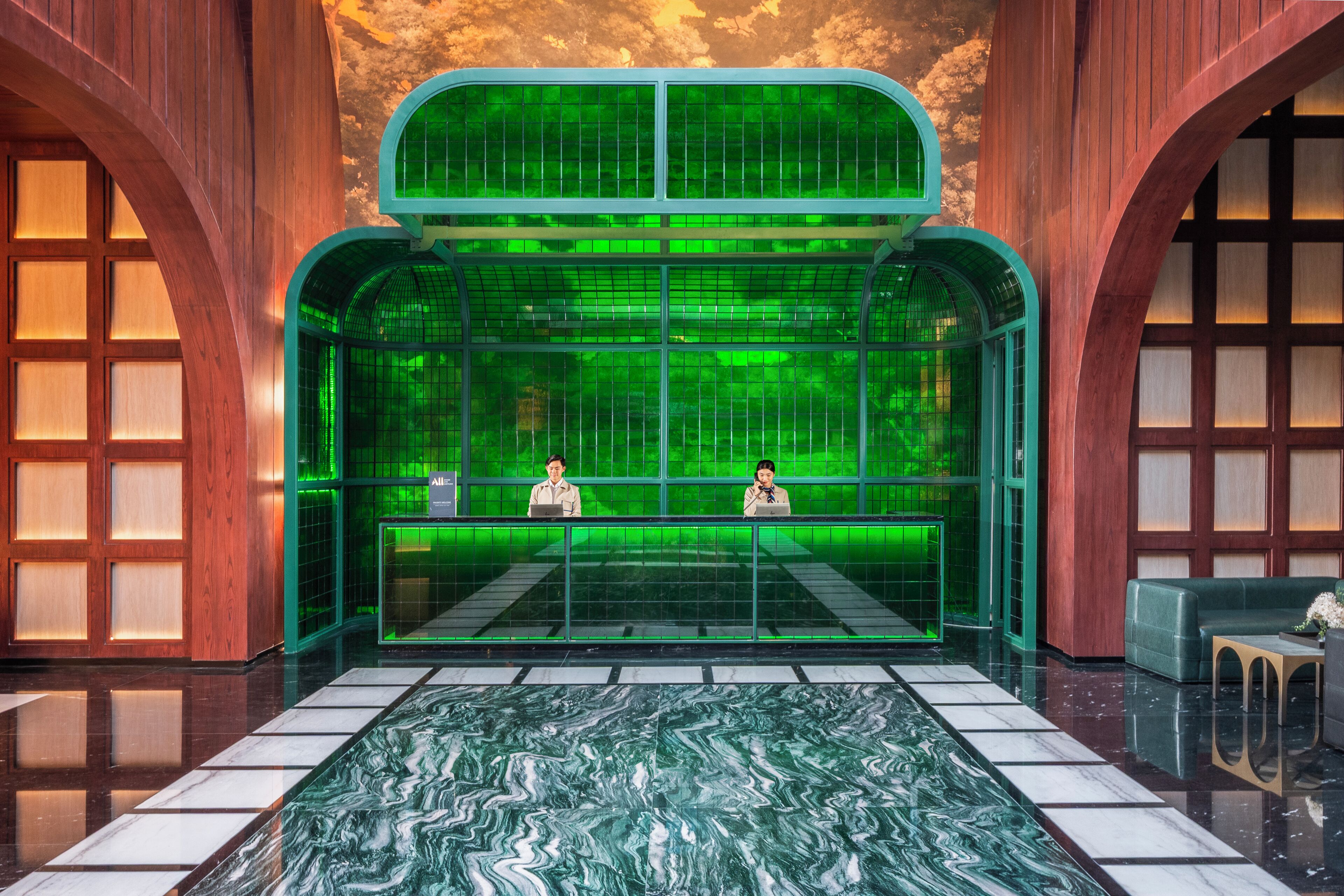 A lobby with a green glass enclosure, a marble floor, and wooden paneling.