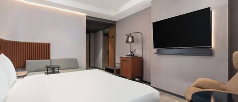 Une chambre d’hôtel moderne avec un grand lit, un téléviseur fixé au mur, un canapé, une petite table et un meuble.
