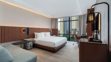 Habitación de hotel moderna con una cama grande, un escritorio, una silla y vistas a la ciudad a través de amplios ventanales.
