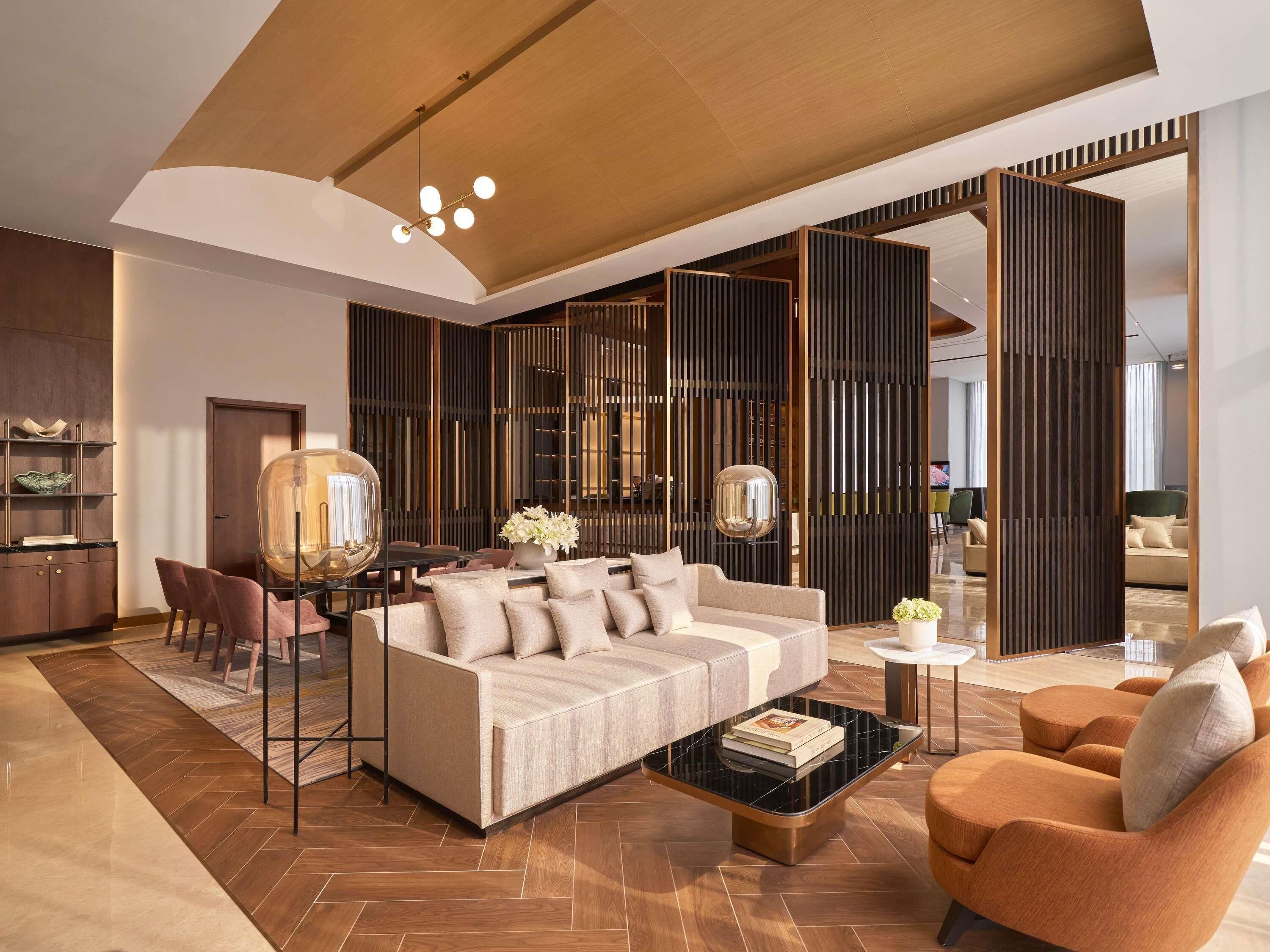 A modern living room with a sofa, coffee table, and chairs, a dining area with a table and chairs, and a large decorative mirror.
