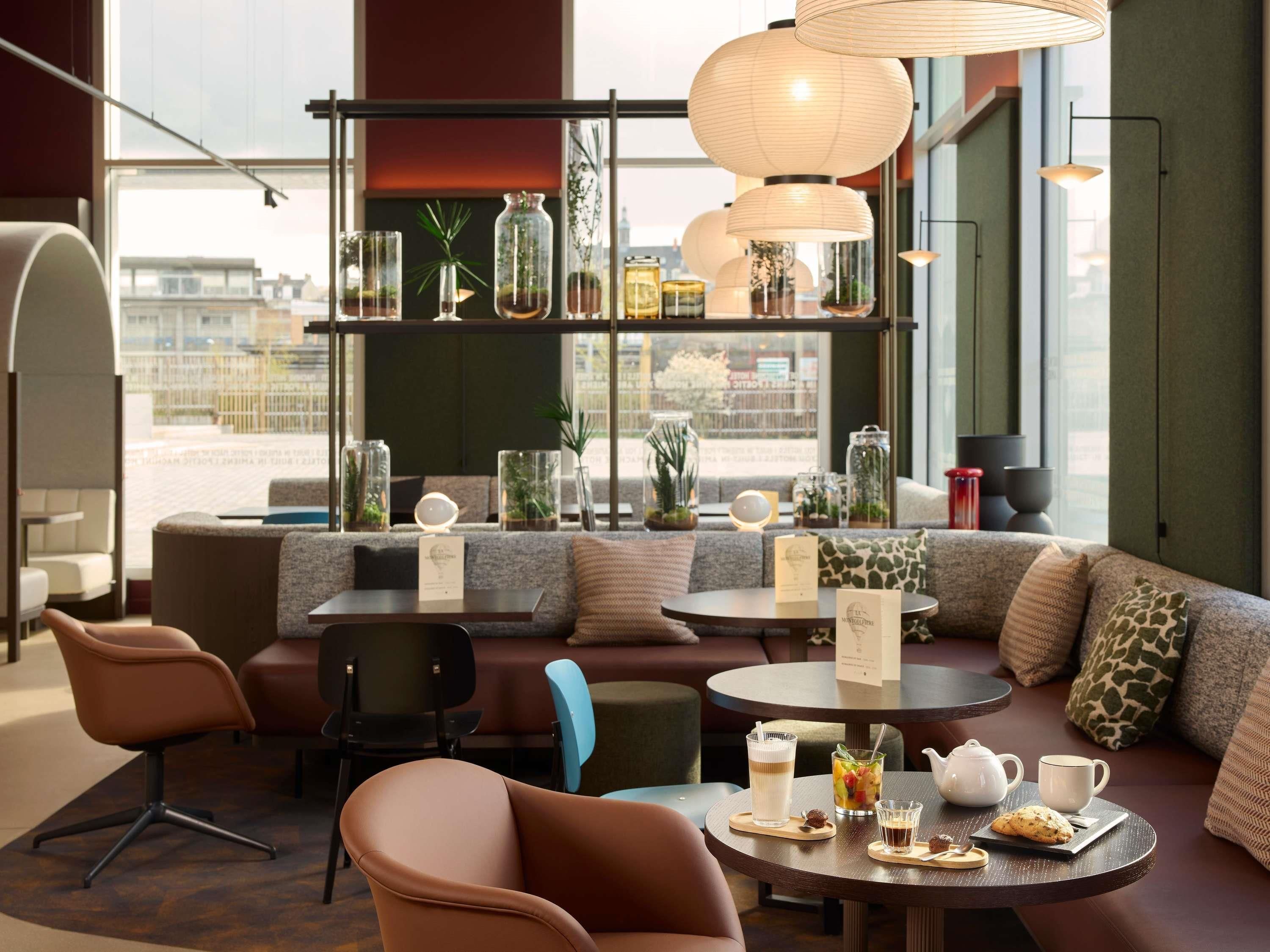 A modern cafe interior with seating arrangements, a coffee table with a teapot and cups, and a city view through large windows.