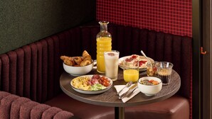 A dining table with breakfast items, a bottle of orange juice, and a glass of milk in a corner booth with a red cushioned seat. - You Hotel Amiens - Handwritten Collection (Amiens)