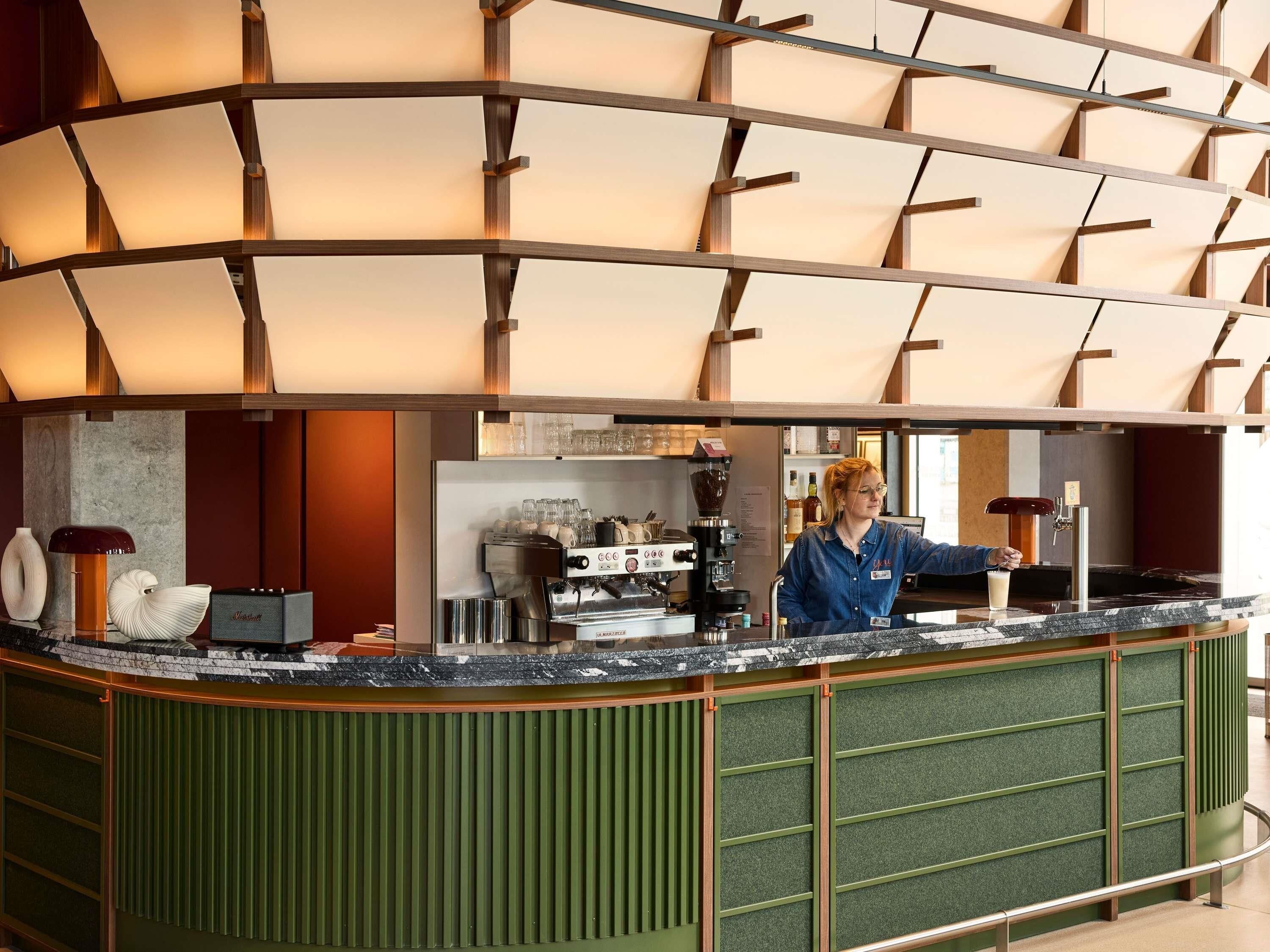 Un moderno espacio de bar con una barra curva, máquinas de café espresso y un barista.