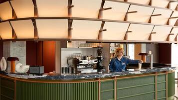 Un moderno espacio de bar con una barra curva, máquinas de café espresso y un barista.
