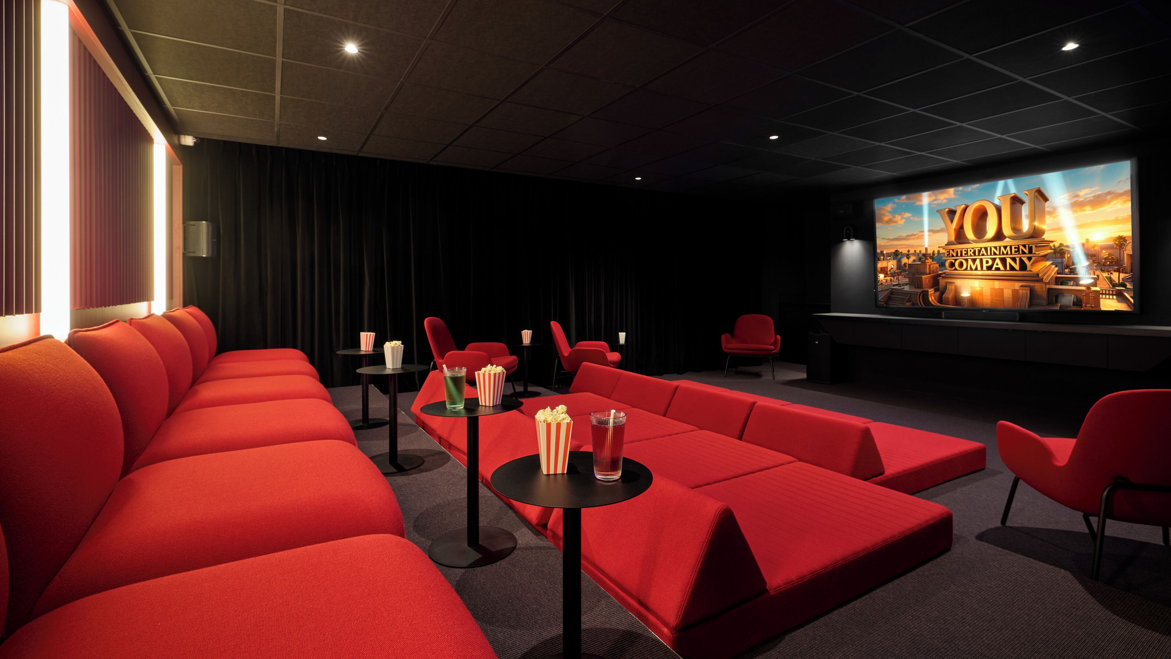 Une salle de cinéma avec des sièges rouges, un écran affichant le nom « YOU ENTERTAINMENT COMPANY » et un projecteur.