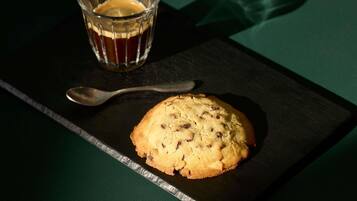 Una galleta sobre un plato de pizarra oscura con una cuchara a un lado, y un vaso de té sobre una mesa verde.