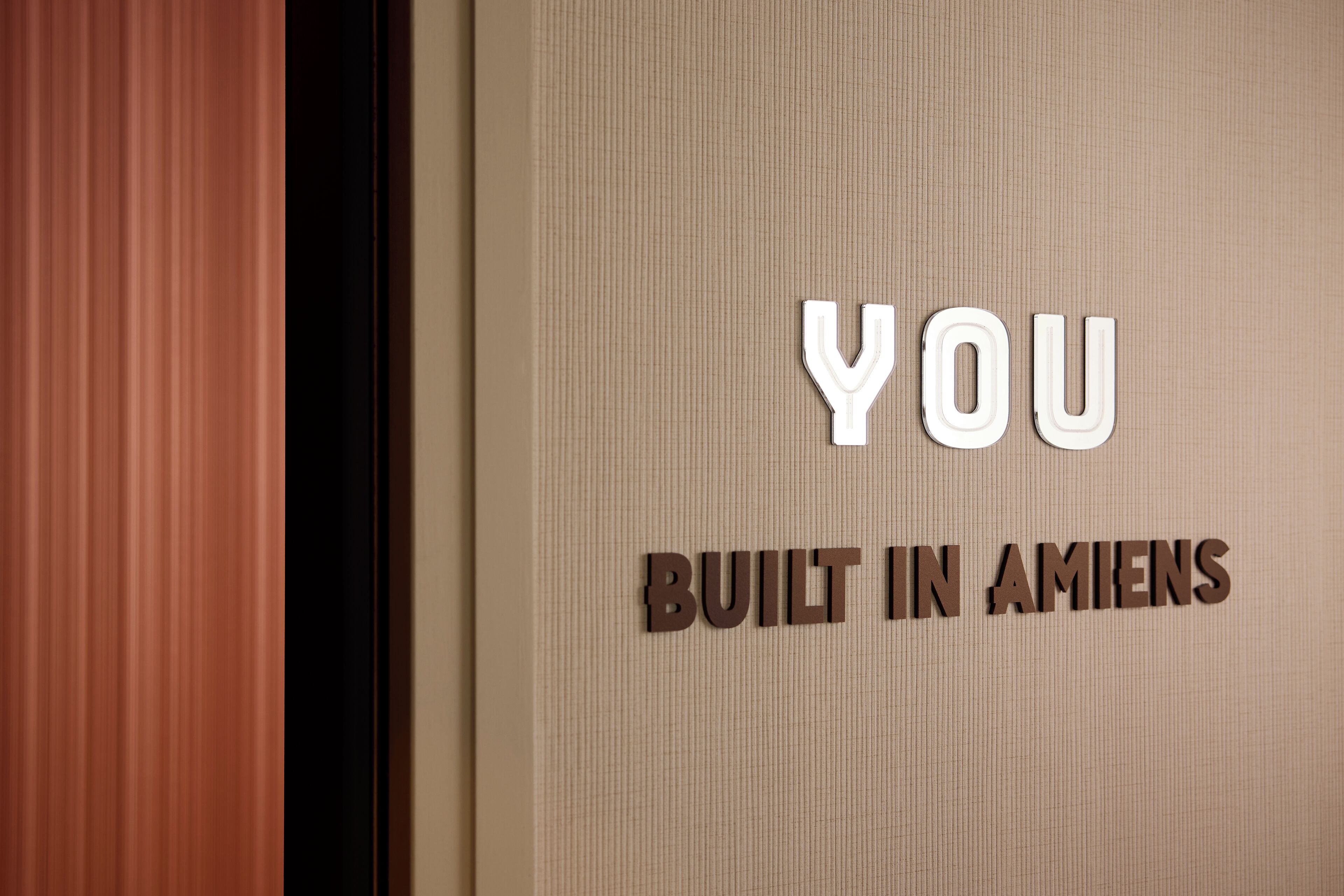 A sign with the text "YOU BUILT IN AMIENS" on a textured wall.