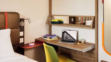 A modern hotel room with a bed, a desk with a laptop, books, and a chair.
