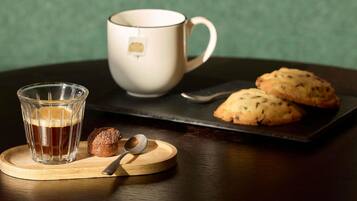 A glass of amber liquid, a white mug, and two cookies on a wooden coaster.