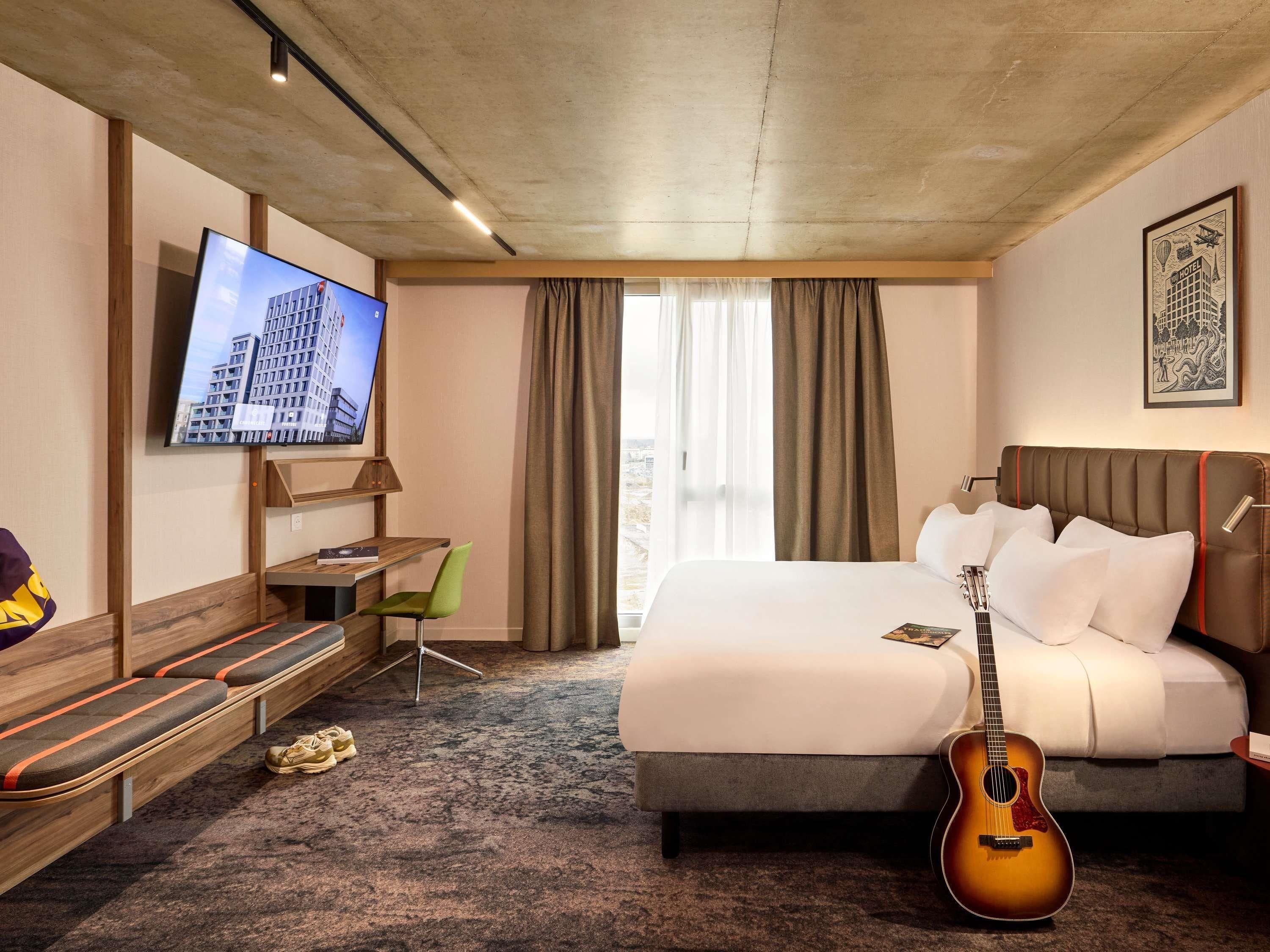 Une chambre d’hôtel avec un lit, une télévision, une guitare, un bureau et une chaise.