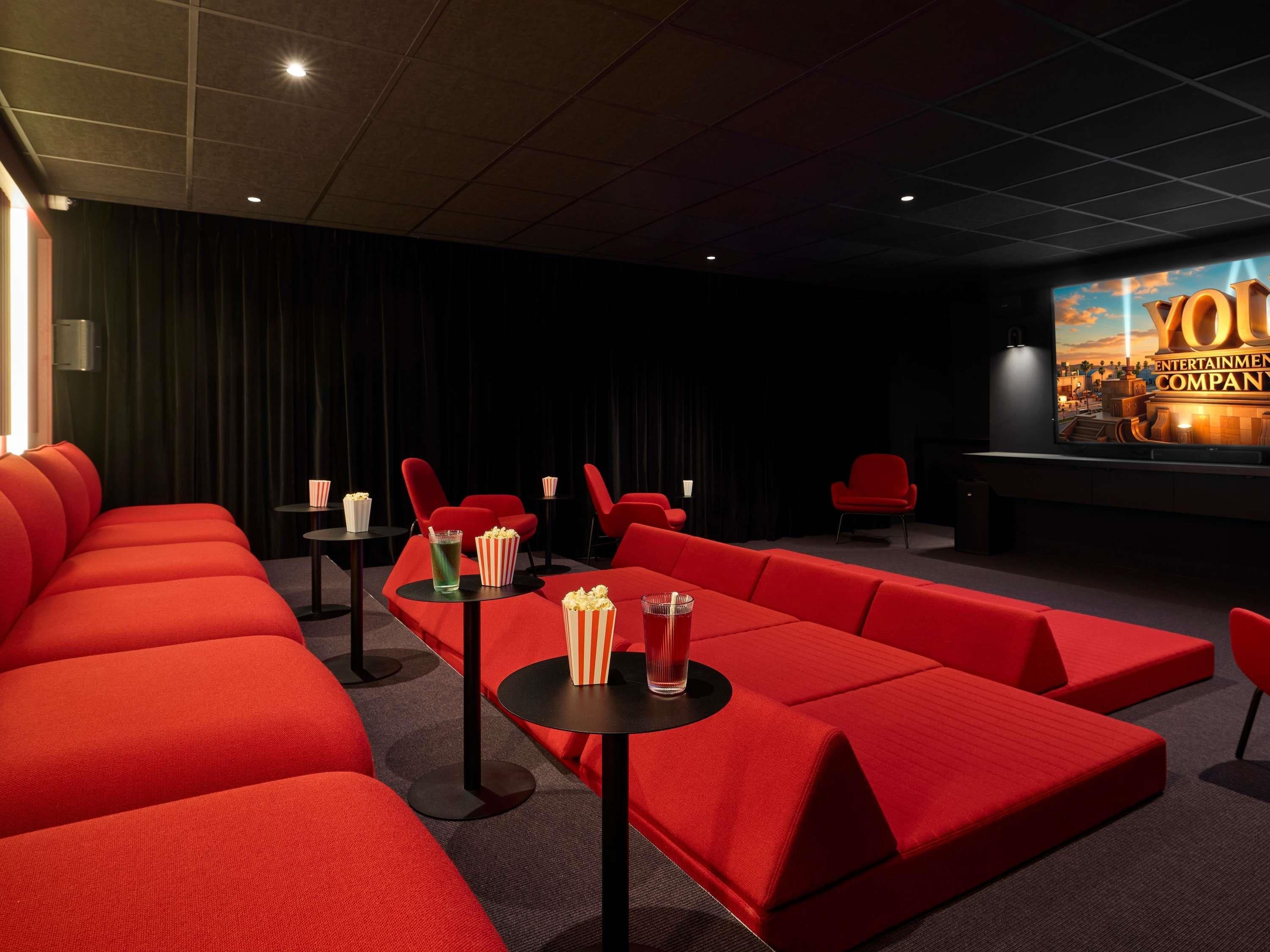 A movie theater with red seating, popcorn, and drinks on tables.