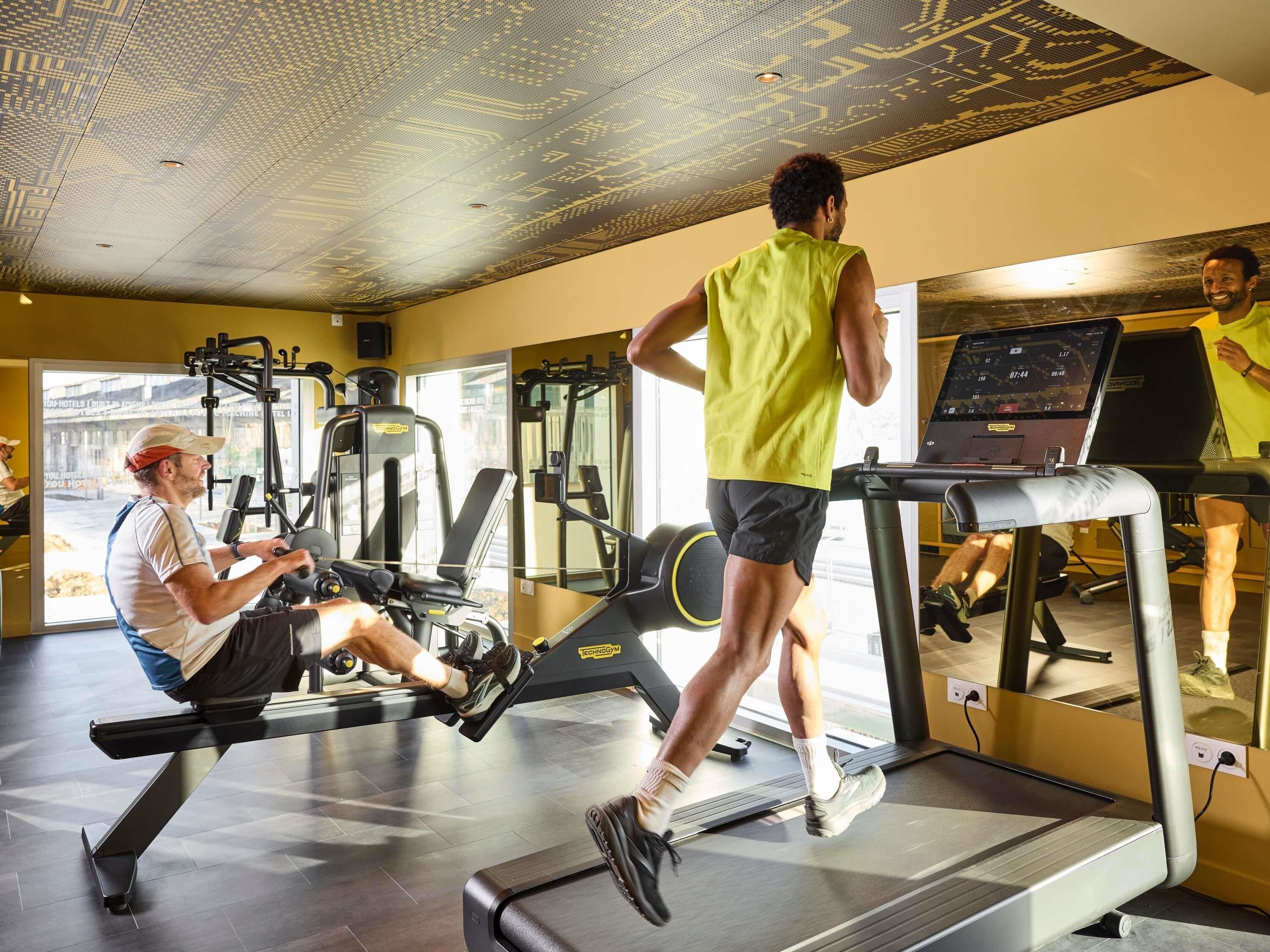 Un gimnasio con equipamiento de ejercicio, una cinta de correr y un espejo que refleja el espacio.