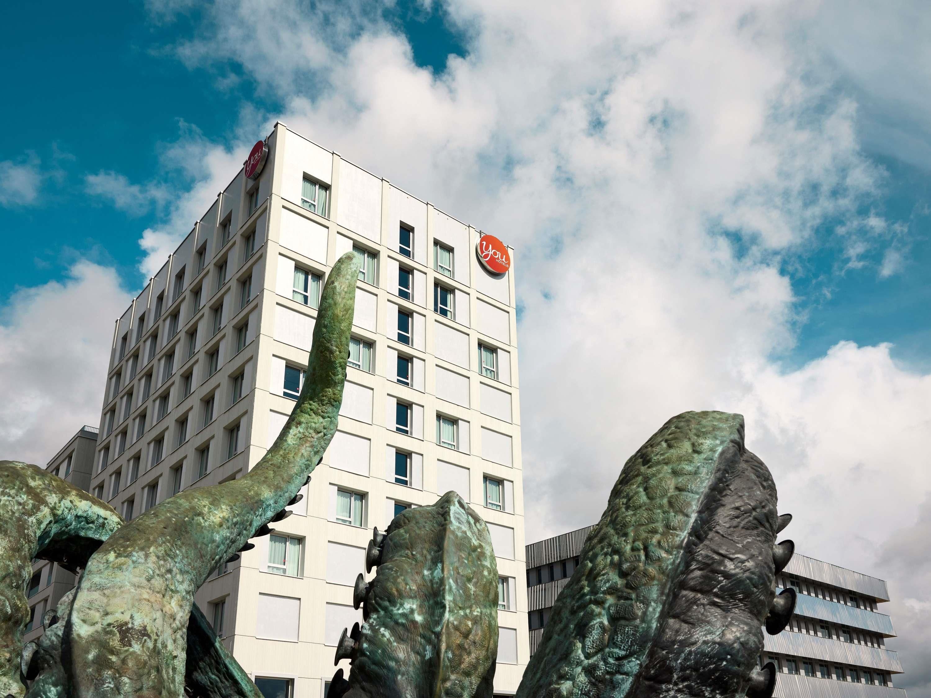 A hotel building with a modern design, featuring a prominent red logo on the top.