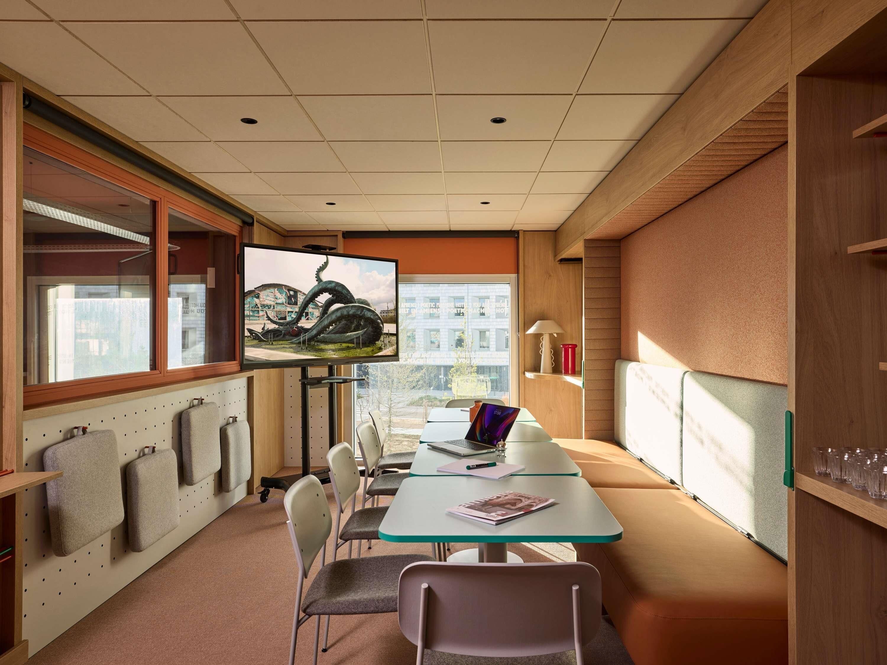 A conference room with a large flat-screen TV, a laptop, and a table with chairs.