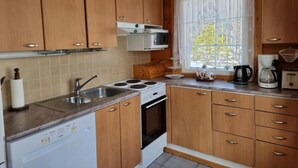 A kitchen with wooden cabinets, a stove, a sink, and a window with a view of greenery.