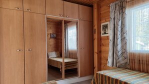 A wooden cabin room with a bed, a wardrobe, and a window with curtains.
