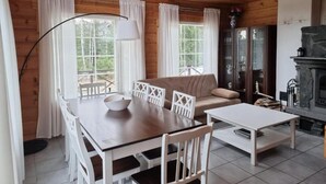 A cozy cabin interior with a wooden dining table, white chairs, a sofa, and a fireplace.