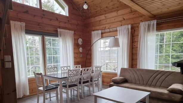 A cozy cabin interior with a dining area, sofa, and large windows.