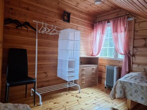 Une pièce de cabane en bois comprenant un lit, une commode, une chaise, un étendoir et un radiateur.