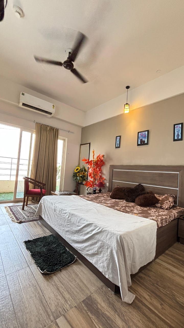 A bedroom with a bed, a ceiling fan, an air conditioning unit, a window with curtains, and a view of the outdoors.
