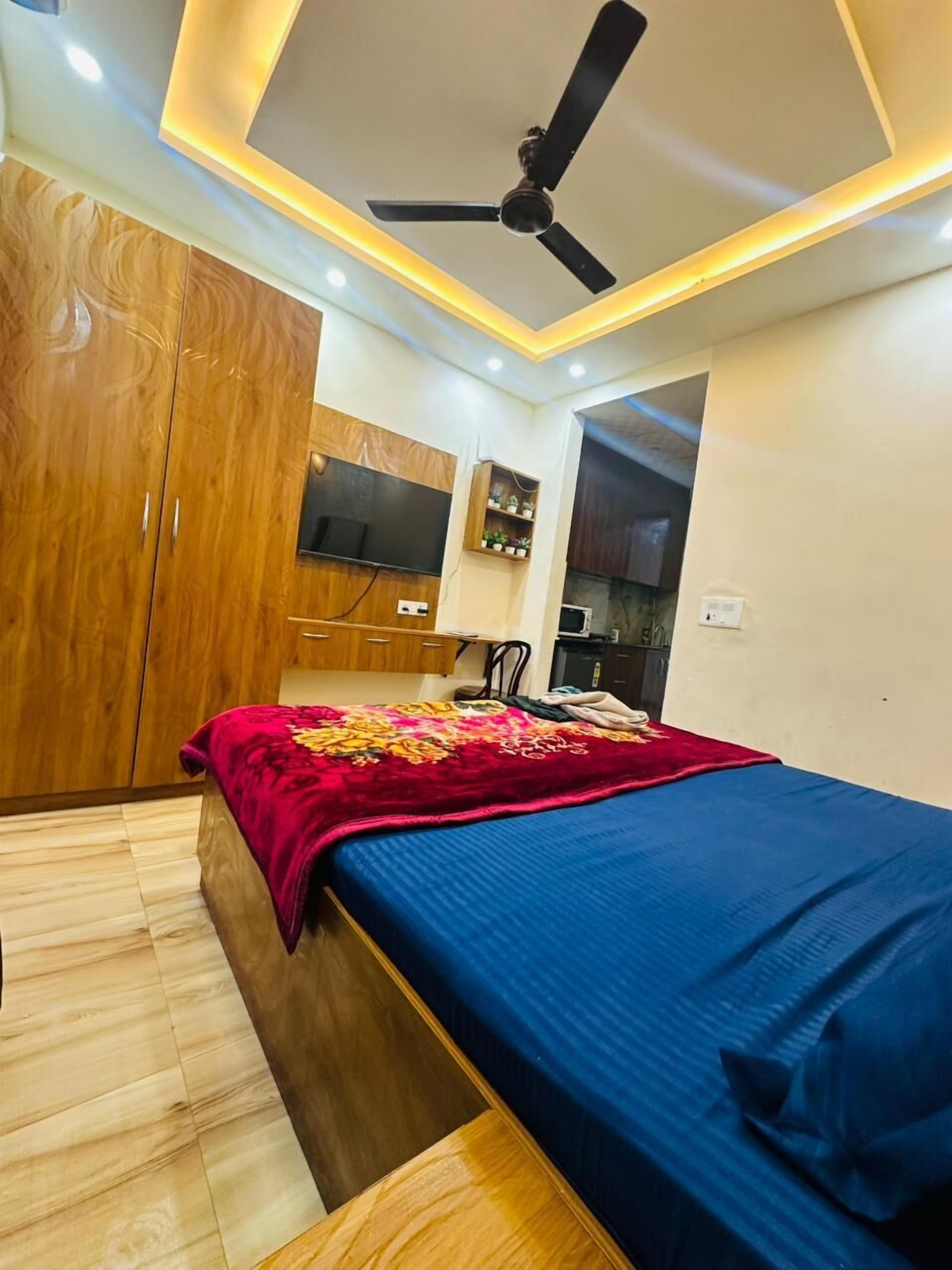 A bedroom with a bed, wardrobe, ceiling fan, and a small kitchenette area.