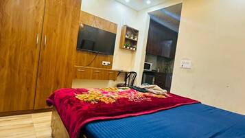 A bedroom with a bed, wardrobe, ceiling fan, and a small kitchenette area.