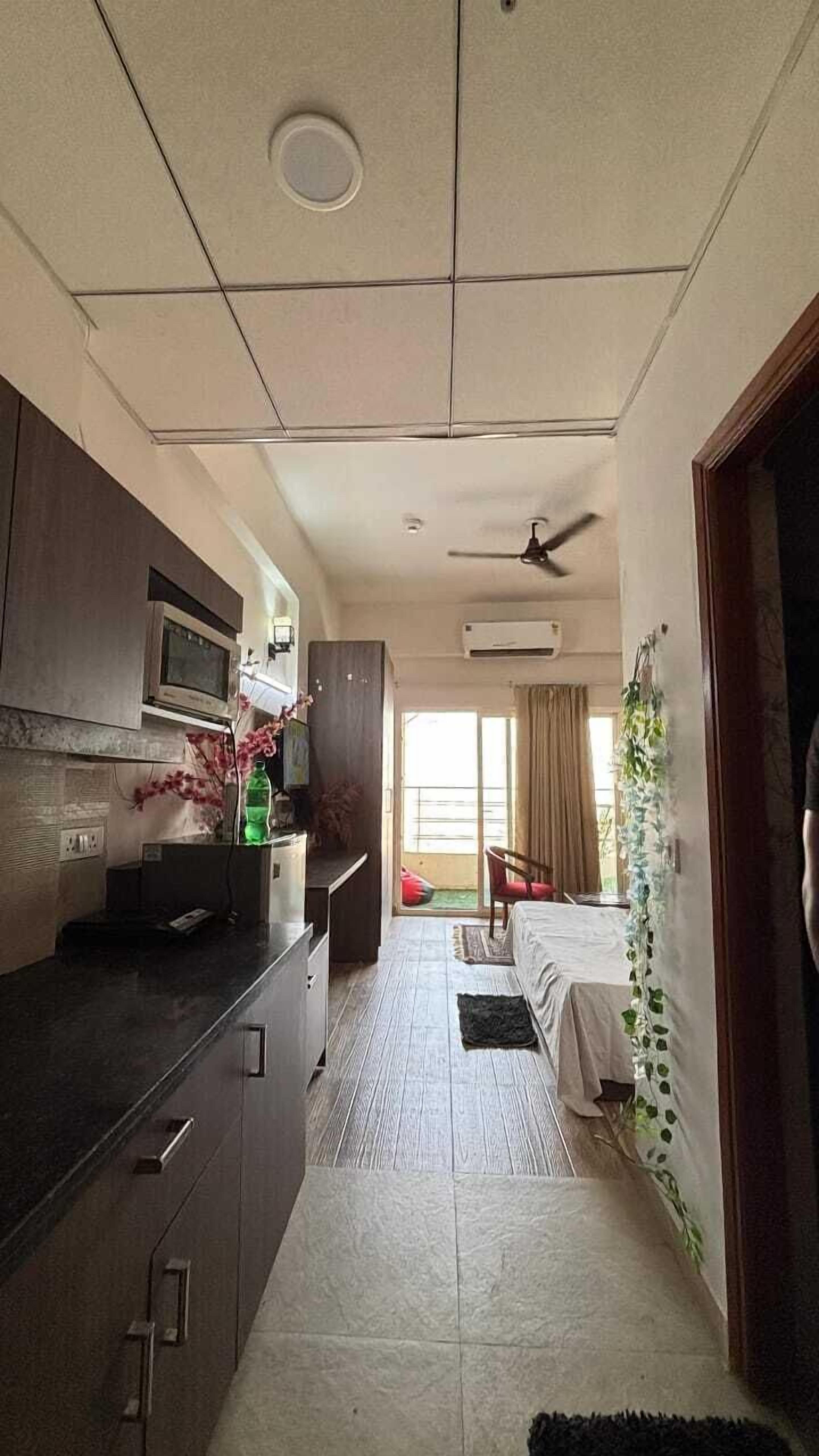 A compact hotel room with a kitchenette, a ceiling fan, a bed with a view, and a small balcony.