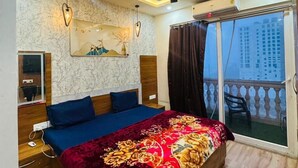 A bedroom with a large bed, a ceiling fan, a wall-mounted air conditioner, and a view of the outside balcony. - High Sky In (Greater Noida)