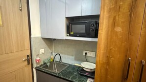 A compact kitchen with grey cabinets, a microwave, a sink, and a wooden door. - High Sky In (Greater Noida)
