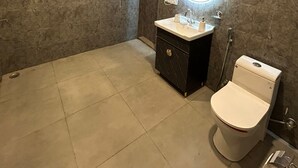 A bathroom with a marble wall, a sink with a mirror, a toilet, and a shower area. - High Sky In (Greater Noida)